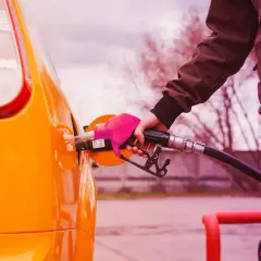 Mano con guanto rosa inserisce la pompa di benzina nel serbatoio di un'auto arancione. Il **consumo auto** è una spesa da considerare.