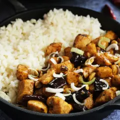 Pyszny kurczak kung pao z ryżem, orzeszkami ziemnymi i szczypiorkiem w żeliwnej patelni.