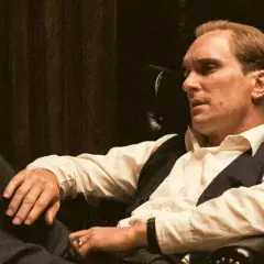 Robert Duvall jako Tom Hagen w fotelu, zamyślony, w białej koszuli i kamizelce.