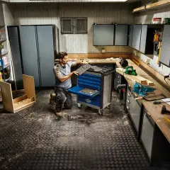 Mann richtet seine Werkstatt ein, sortiert Werkzeuge in einen blauen Werkzeugwagen. Alles ist bereit für das nächste Projekt.