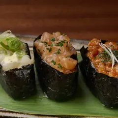 Drei Gunkan-Maki-Sushi mit Lachs, Garnelen und Fisch, garniert mit Frühlingszwiebeln und Kräutern.