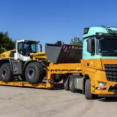 Pomarańczowo-miętowa ciężarówka transportuje ładowarkę kołową Liebherr na niskopodwoziowej przyczepie. Efektywny transport maszyn budowlanych.