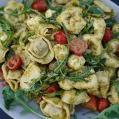 Mediterraner Salat mit Tortellini, Mozzarella-Bällchen, Kirschtomaten und Rucola, verfeinert mit Pesto.