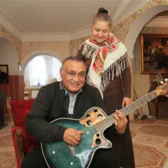Uśmiechnięty mężczyzna gra na gitarze, a za nim stoi kobieta. Nie wiadomo, ile lat ma Don Vasyl, ale wygląda na szczęśliwego.