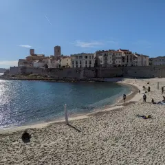 Sonniger nizza strand mit Menschen, die sich entspannen, und einer historischen Stadt im Hintergrund.