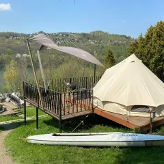 Namiot typu glamping camp z widokiem na jezioro i wzgórza. Na tarasie stolik i krzesło. Obok leży kajak.