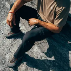Man sitting on rocks, wearing black pants and hiking shoes. The shoes are grey with orange laces, perfect for schoenen oprekken on any terrain.