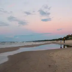 Zachód słońca nad morzem w Łebie. Spokojna plaża, kilka osób spaceruje, a w oddali widać budynek z czerwonym dachem. To piękne łeba atrakcje poza sezonem.