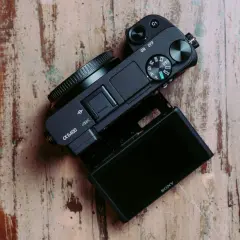 Czarny aparat Sony α6400 z uchylnym ekranem leży na drewnianym blacie. Idealny do testów i vlogowania.