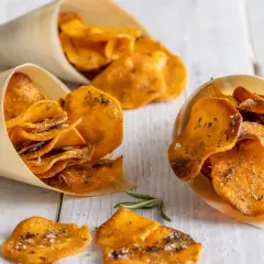 Croccanti patate dolci in padella, condite con erbe aromatiche e sale, servite in coni di legno.