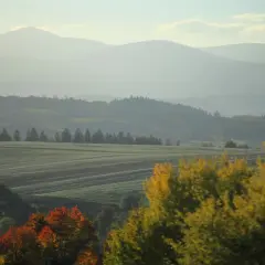 Mglisty poranek na zboczach góry Witosza. Pola i lasy w jesiennych barwach, w oddali majaczą kolejne pasma górskie.