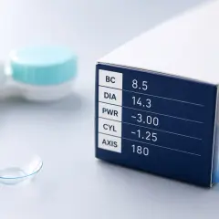 Pudełko z soczewkami kontaktowymi, na którym widnieją parametry: BC 8.5, DIA 14.3, PWR -3.00, CYL -1.25, AXIS 180. Obok pojemnik na soczewki i pojedyncza soczewka.