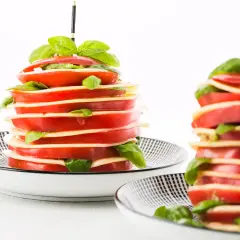 Torres de tomates y mozzarella con albahaca, unos entrantes típicos de Francia, servidos en platos con diseño geométrico.