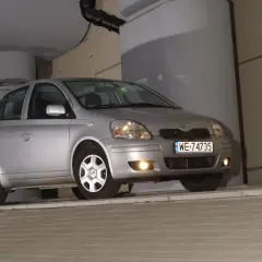 Srebrny Toyota Yaris 1.4 D4D, z tablicą WE 74735, zaparkowany pod betonowym zadaszeniem.