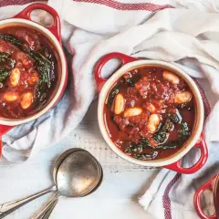 Due ciotole rosse con zuppa di cavolo nero e fagioli, pronte per essere gustate.
