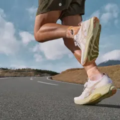 Biegacz w lekkich, białych butach do maratonu pokonuje krętą drogę na tle górskiego krajobrazu.