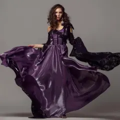 A model in a flowing purple gown and black lace sleeves poses for studio fashion photography.