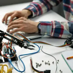 Programista tworzy automatyzację procesów, programując ramię robota na laptopie.