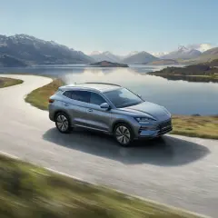 Srebrny BYD Song Plus sunie po krętej drodze nad jeziorem, w tle majestatyczne góry.