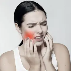 Mujer con dolor, tocándose la mejilla donde se ve un bulto mejilla interna enrojecido.