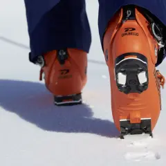 Botas de esquí naranjas Dalbello con suela de **grip walk** en la nieve, listas para la aventura.