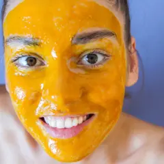 Uśmiechnięta twarz z maseczką z kurkumy, która rozjaśnia cerę. Naturalne piękno w domowym spa.