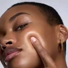Piel oscura con un brillo dewy, resaltando sus pómulos y labios.