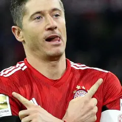 Robert Lewandowski w czerwonej koszulce Bayernu z naszywką Bundesligi, wykonuje gest radości po strzelonej bramce.