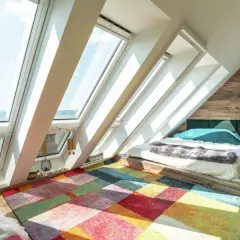 Un letto accogliente in una soffitta luminosa, con un tappeto colorato che dona un significato di gioia e calore.