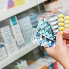 Manos sostienen blísteres de pastillas, eligiendo entre paracetamol o ibuprofeno.