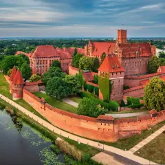 Zamek w Malborku, potężna twierdza z czerwonej cegły, otoczona zielenią i wodą, zaprasza do zwiedzania.