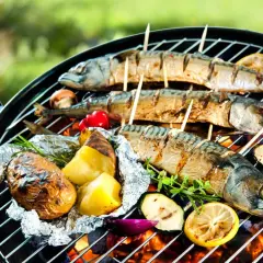 Drei ganze Makrelen werden auf einem Grill mit Kartoffeln, Tomaten und Zucchini gegrillt.