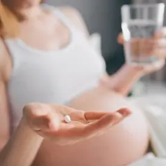 Kobieta w ciąży bierze tabletkę i popija ją wodą, dbając o prawidłowe ciśnienie w ciąży.