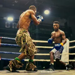 Two boxers face off in a ring, one in camouflage shorts, the other in blue. Their boxing opponent is ready for the fight.