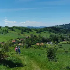Dwie dziewczynki wędrujące po zielonych wzgórzach Gór Sowich z widokiem na wieś.