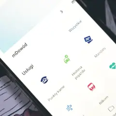 Na ekranie telefonu widać aplikację z opcjami: mDowód, Usługi, Punkty karne, Historia pojazdu, Mandaty. Możesz tu sprawdzić mandaty.