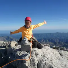 Szczęśliwa alpinistka na szczycie góry, z widokiem na pasmo górskie. W tle widać morze. To szczyt Naranjo de Bulnes.