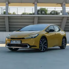 Nowy żółty Toyota Prius z nowoczesnym designem stoi na betonowym placu przed trybunami stadionu.