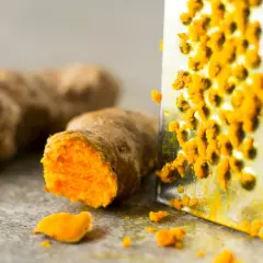 Frisch geriebene Kurkuma auf einem Metallreibe. So lässt sich die leuchtend orangefarbene Wurzel für die Lagerung vorbereiten.