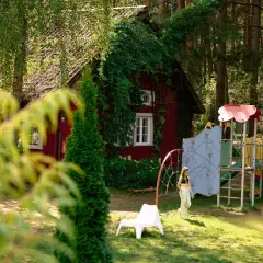 Dziewczynka na placu zabaw przy czerwonym domku w lesie. Idealne fajne miejsce na Mazurach z dzieckiem.
