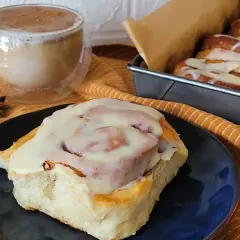 Pyszne cynamonki bez jajek polane lukrem, obok kubek kawy i gwiazdki anyżu. Idealne na jesienny deser.
