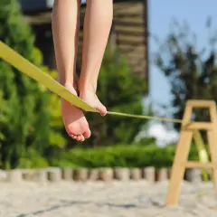 Füße balancieren auf einer gelben Slackline, die an einem Holzgestell befestigt ist.