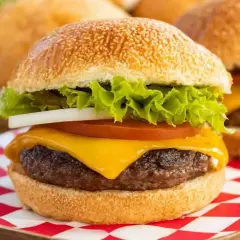 Soczyste mięso na burgery z serem, sałatą, pomidorem i cebulą, podane na kratkowanej serwetce.