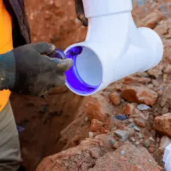 Instalator nakłada fioletowy klej na rurę PVC, przygotowując ją do montażu. Brak odpowietrzenia pionu może prowadzić do problemów z instalacją.