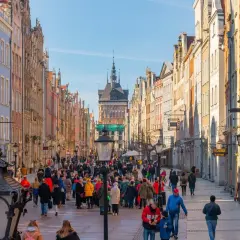 Tłum ludzi spaceruje ulicą Długą na gdańskiej starówce, podziwiając kolorowe kamienice i zabytkową architekturę.