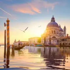 Gondola naviga sul Canal Grande al tramonto, con la maestosa Basilica di Santa Maria della Salute che domina lo skyline.