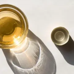 Ein Glas mit goldenem Apfelessig steht neben seinem Deckel. Sonnenschein wirft interessante Schatten. Bereit, Apfelessig zu trinken.