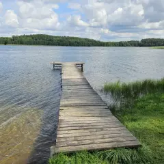 Drewniane molo prowadzi do spokojnego jeziora, otoczonego zielonymi lasami. To idealne miejsce na wypoczynek na łonie natury, prawdziwy kamień krajeński.