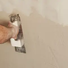 Mano che esegue la rasatura di un muro con una spatola, creando una finitura liscia e uniforme.