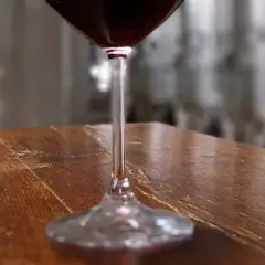 Bottiglie di Vino Nobile di Montepulciano e un calice di rosso, in un'ambientazione che evoca le cantine delle province di Siena.
